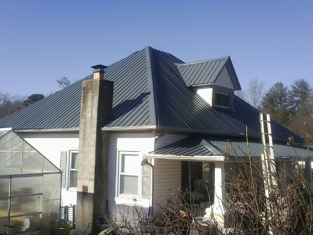 Dark blue standing seam metal roof on a white farmhouse with dormer — Slate & Tile Roof Repair by Roofing Brothers in Parsons