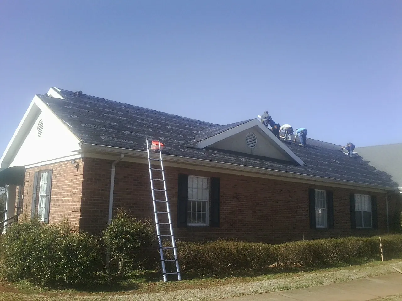 Crew tearing shingles off a brick ranch roof with a ladder set — Metal Roof Repair work by our crew in Parsons
