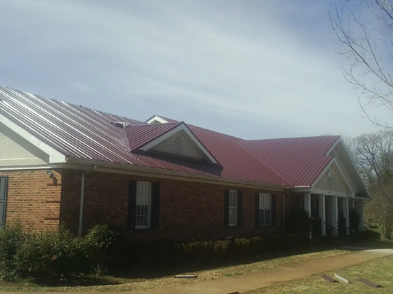 Red metal roof with gabled entries on a long brick building, from a Hail Damage Roof Repair job in Parsons