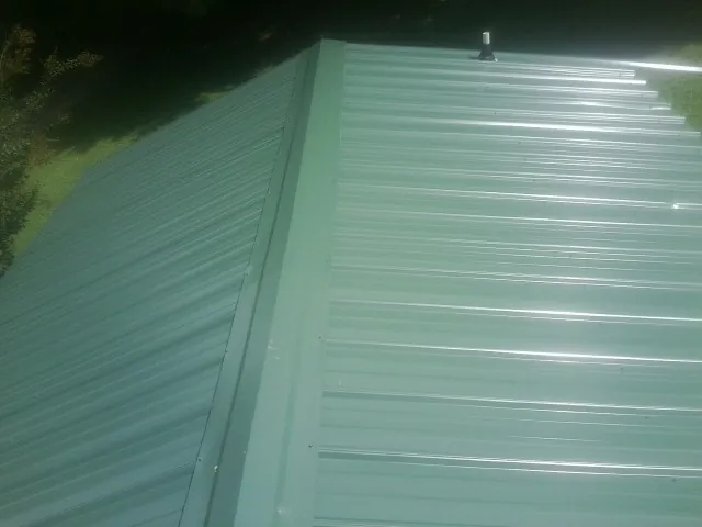 New green metal panels meeting at the ridge of a roof — Flat Roof Repair work by our crew in Parsons