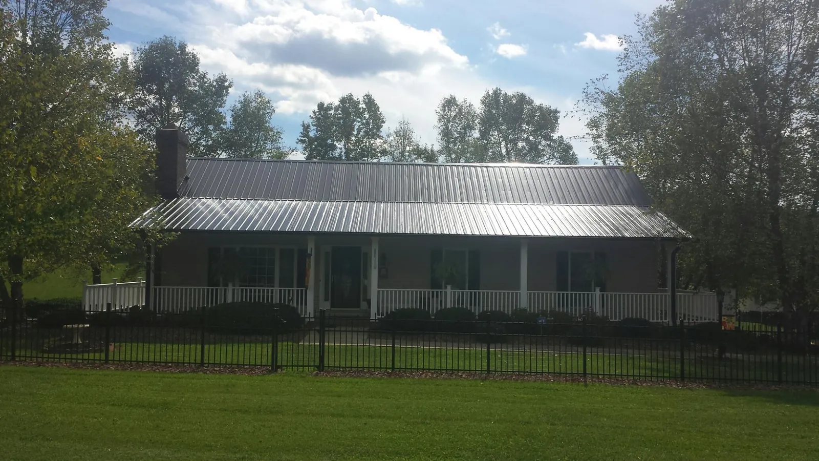 Gray metal roof on a brick ranch with a full width front porch — Gutter Guard Installation work by our crew in Parsons
