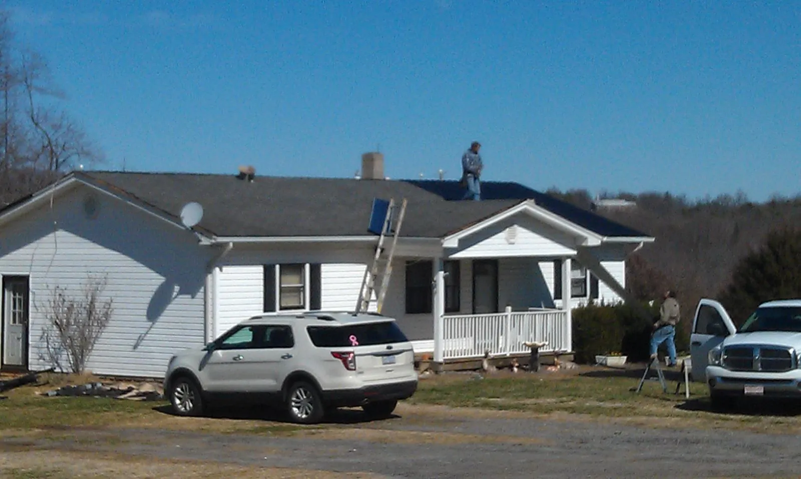 Roofers stripping shingles from a white ranch house roof in Parsons