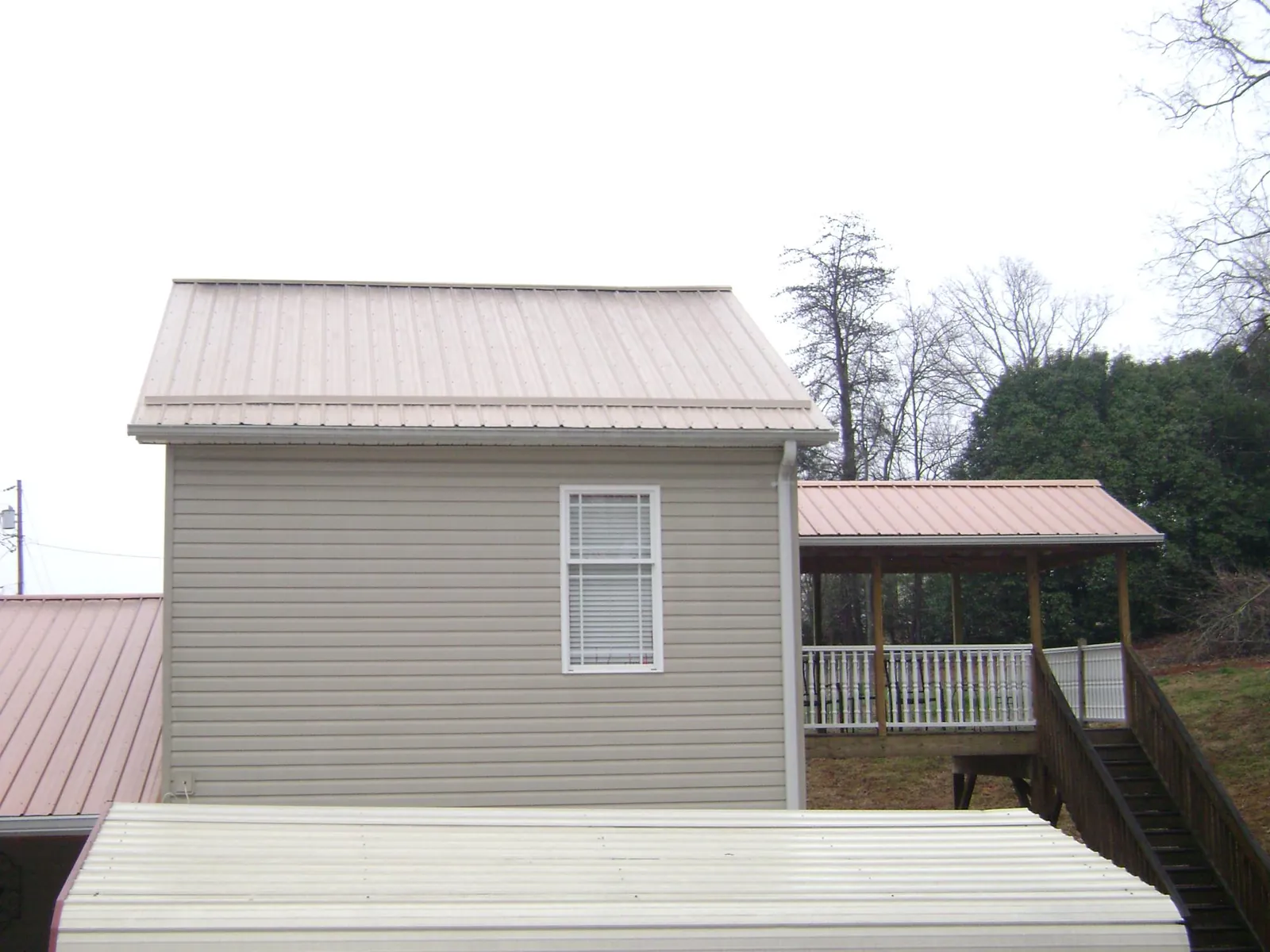Tan metal roofs on a two story addition and attached porch, from a Roof Replacement job in Parsons